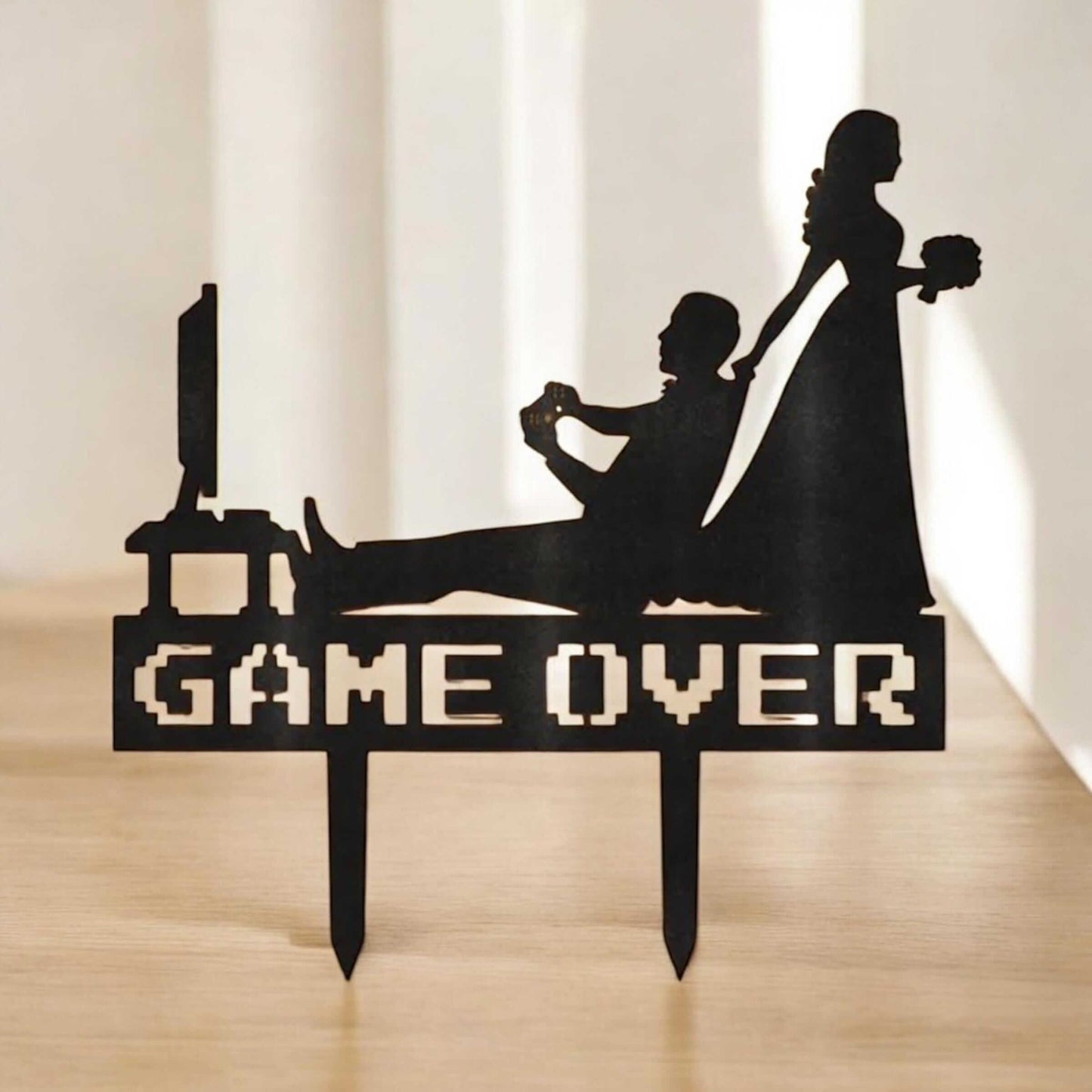 Funny gamer wedding cake topper featuring a groom playing video games and a bride pulling him away with 'GAME OVER' sign.