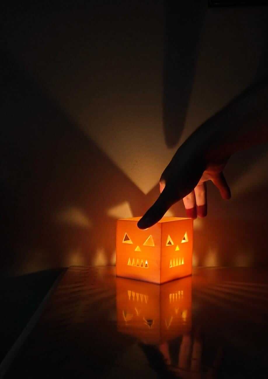 jack-o-lantern candle holder casting spooky shadows with a hand reaching for it, perfect for Halloween decor.